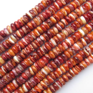 Peut inclure: Gros plan sur des brins de perles en coquillage d'hu&icirc;tre &eacute;pineuse. Les perles sont un m&eacute;lange de couleurs brun rouge&acirc;tre, orange et blanc. Les perles sont petites, rondes et de forme l&eacute;g&egrave;rement irr&eacute;guli&egrave;re. Les perles sont enfil&eacute;es en rang&eacute;e.
