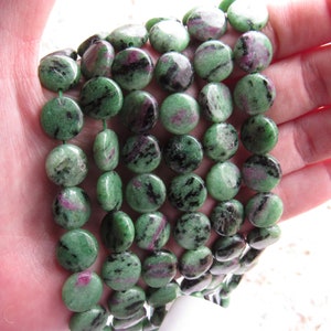 Könnte beinhalten: Eine Strähne aus grünen, schwarzen und rosafarbenen Edelsteinperlen. Die Perlen sind rund und flach und auf einem durchsichtigen Faden aufgefädelt.