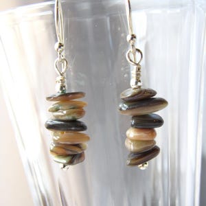 Puede incluir: Un par de pendientes de plata con una pila de cuentas de color marrón, beige y negro con forma de concha.