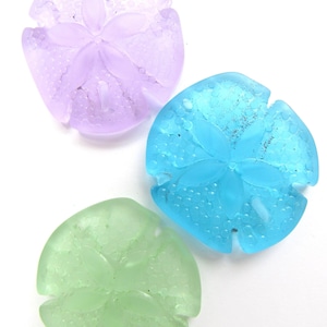 May include: Three sand dollar shaped glass ornaments in purple, blue, and green.