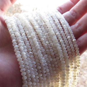 May include: A strand of white mother of pearl beads. The beads are round and have a slight iridescent sheen.