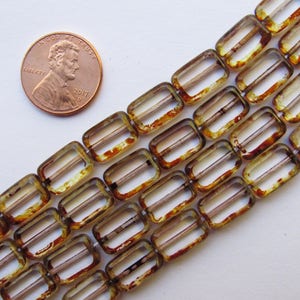 May include: A strand of brown and clear glass beads with a rectangular shape and a hole in the center. The beads have a mottled, translucent appearance.