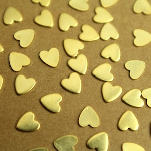 May include: A scattering of gold heart-shaped metal charms on a brown surface.