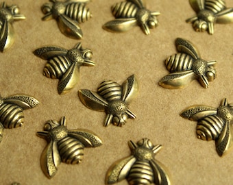 May include: A collection of gold-toned metal bee figurines arranged on a brown surface. The bees have detailed wings and bodies.