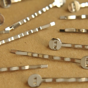 May include: A close-up of a group of silver hair clips with round, decorative ends. The clips are arranged on a brown surface.