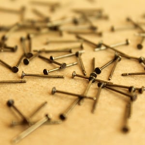 May include: A close-up of a pile of small, bronze-colored metal pins with pointed ends. The pins are scattered on a brown surface.