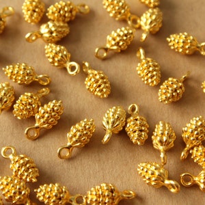 May include: A collection of gold-toned metal pine cone charms with a loop for attaching to jewelry or other crafts.