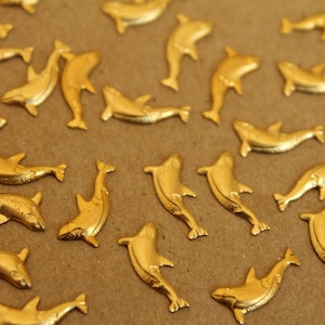 Op de afbeelding: Een verzameling gouden dolfijnbeeldjes verspreid over een bruin oppervlak. De dolfijnen kijken allemaal in verschillende richtingen en zijn gemaakt van glanzend metaal.