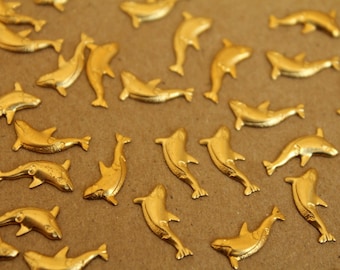 May include: A collection of gold-colored dolphin figurines scattered on a brown surface. The dolphins are all facing different directions and are made of a shiny metal.