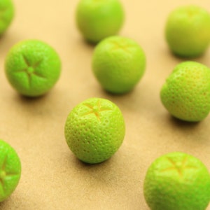 May include: A group of ten green limes arranged on a light brown surface. The limes are all roughly the same size and shape, and they have a slightly bumpy texture.