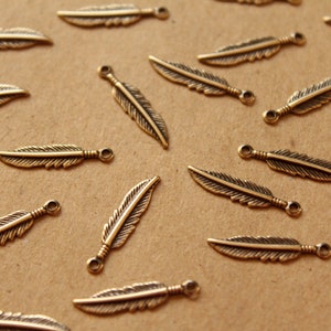 May include: A collection of gold-toned metal feather charms. The feathers are all the same size and shape, and they have a slightly textured surface.