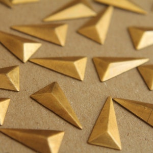 Puede incluir: Primer plano de un grupo de formas triangulares de metal de color dorado esparcidas sobre una superficie marrón. Las formas son todas del mismo tamaño y tienen un acabado brillante.