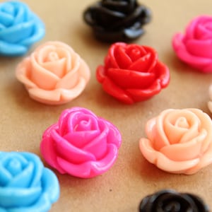 Op de afbeelding: Assortiment van kleurrijke plastic rozenbloemversieringen in verschillende kleuren, waaronder roze, blauw, rood, wit en zwart.