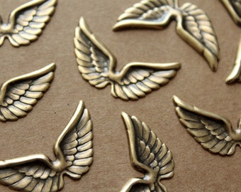 May include: A collection of gold-toned metal angel wings with a detailed design. The wings are arranged on a brown surface.