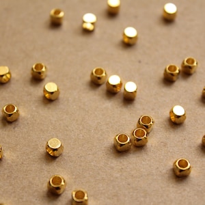 May include: A close-up of a group of gold-colored metal beads scattered on a brown surface. The beads are round and have a textured surface.