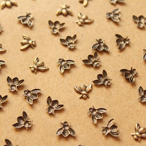 May include: A collection of small, gold-toned metal bee charms scattered on a brown surface. The bees are all facing different directions and have a detailed design.