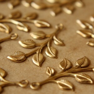 May include: A collection of gold-toned metal leaf branch charms. Each charm features a delicate branch with multiple leaves.