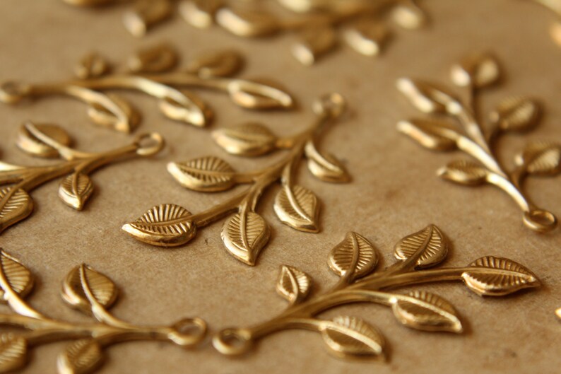May include: A collection of gold-toned metal leaf branch charms. Each charm features a delicate branch with multiple leaves.
