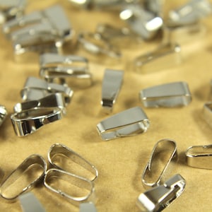 Puede incluir: Primer plano de un grupo de anillos de salto de metal plateado. Los anillos son de varios tamaños y formas, y algunos están abiertos, mientras que otros están cerrados.