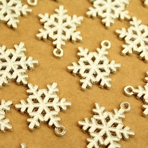 May include: A collection of silver snowflake charms with white enamel. The charms have a loop at the top for hanging.