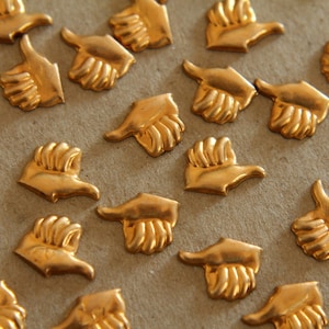 May include: A collection of gold-colored metal thumbs up symbols, arranged on a brown surface. The thumbs up symbols are all facing the same direction, with the thumbs pointing up.
