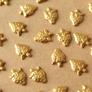 May include: A collection of gold-coloured metal strawberry-shaped embellishments on a brown surface.