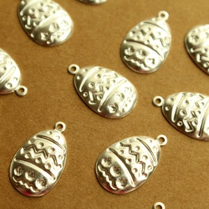 May include: A collection of silver-colored metal egg-shaped charms with an embossed pattern. The charms have a loop at the top for attaching to a necklace, bracelet, or other jewelry.