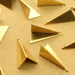 May include: A collection of gold-colored metal triangle shapes with a hole at the top. The triangles are scattered on a brown surface.