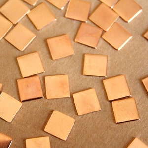 May include: A collection of small, square, copper-colored metal pieces scattered on a brown surface.