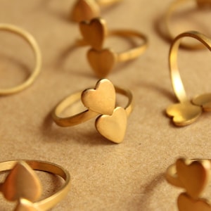 May include: A set of gold-toned rings with heart-shaped designs. The rings are stacked and arranged on a brown surface.