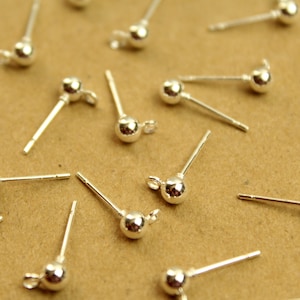 May include: A close-up of silver earring findings with a round ball at the end of the post. The findings are scattered on a brown surface.