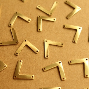 May include: A collection of gold-coloured metal corner brackets, scattered on a brown surface. The brackets are in the shape of a right angle, with two holes on each side.