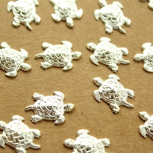 May include: A collection of silver turtle charms, each with a detailed design, scattered on a brown surface.