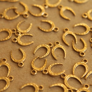 May include: A collection of gold-colored metal horseshoe charms. The charms are scattered on a brown surface.