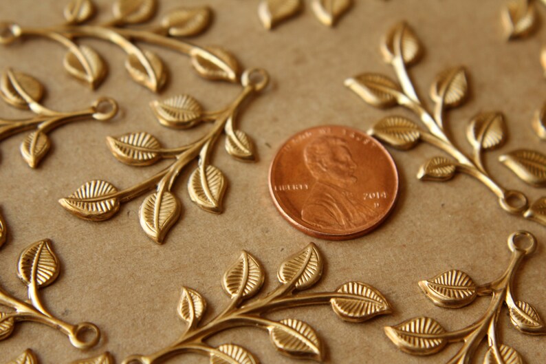 May include: Gold-toned metal leaf sprigs with a penny for scale. The sprigs have a delicate, intricate design and are perfect for adding a touch of elegance to crafts and jewelry.