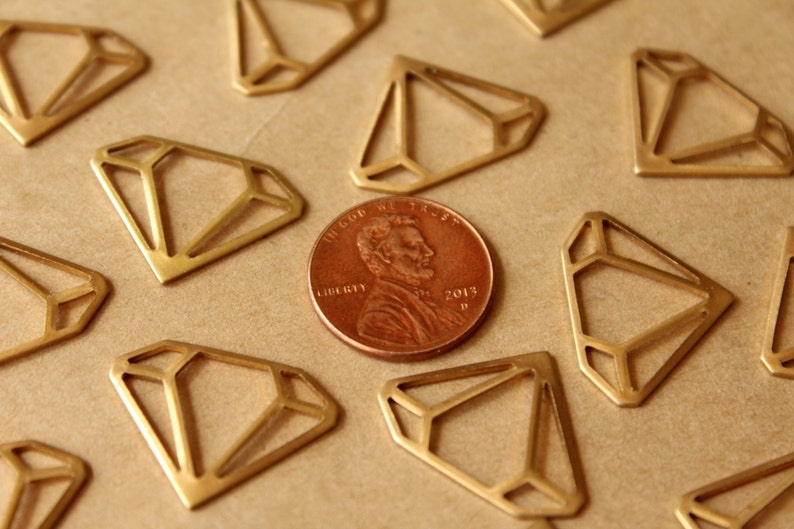 May include: A close-up of a collection of gold-coloured metal diamond shapes on a brown surface. A US penny coin with the words "In God We Trust" and "Liberty" is in the centre of the image.