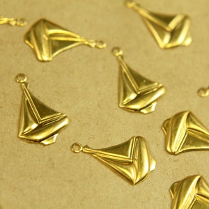 May include: A collection of gold-colored metal sailboat charms. The charms are all the same design, with a simple, stylized sailboat shape. They are arranged on a brown surface.