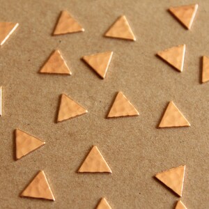 May include: A close-up of a brown surface with 18 small, gold-colored triangle shapes scattered across the surface.