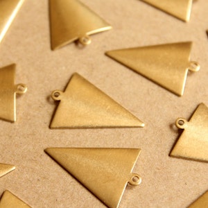 Puede incluir: Un grupo de diez dijes de metal de forma triangular de color dorado con un agujero en la parte superior. Los dijes están dispuestos sobre una superficie marrón.