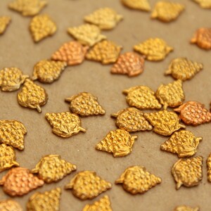 May include: A close-up of a collection of gold-toned metal grape clusters. The clusters are arranged on a brown surface.