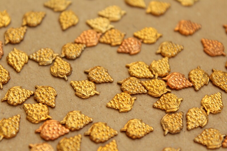 May include: A close-up of a collection of gold-toned metal grape clusters. The clusters are arranged on a brown surface.