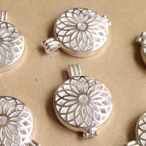 May include: Six silver locket pendants featuring a white, intricate floral design. The lockets are open and have a hinged closure.