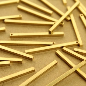 May include: A group of gold-colored metal bars with rounded ends. The bars are scattered on a brown surface.
