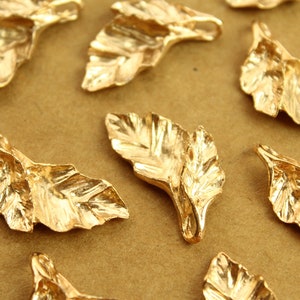 May include: A collection of gold-toned metal leaf charms with a textured surface. The charms are shaped like leaves and have a loop at the top for attaching to jewelry or other crafts.