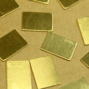 May include: A collection of small, rectangular brass plates, scattered on a brown surface. The plates have a brushed finish and appear to be made of metal.