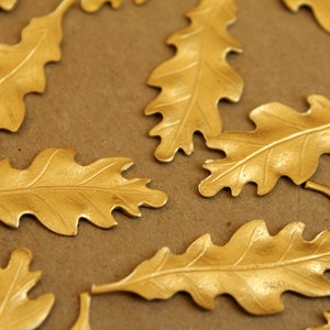 May include: A collection of golden oak leaf decorations. Each leaf has intricate veining and a metallic sheen. They are arranged on a brown surface, suitable for crafting or seasonal displays. The leaves are approximately 10 cm long.
