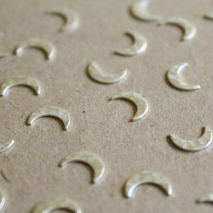 May include: A close-up of a brown surface covered with silver crescent moon charms. The charms are scattered randomly across the surface.