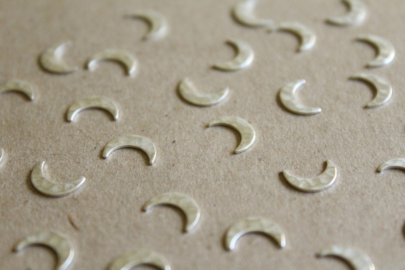 May include: A close-up of a brown surface covered with silver crescent moon charms. The charms are scattered randomly across the surface.
