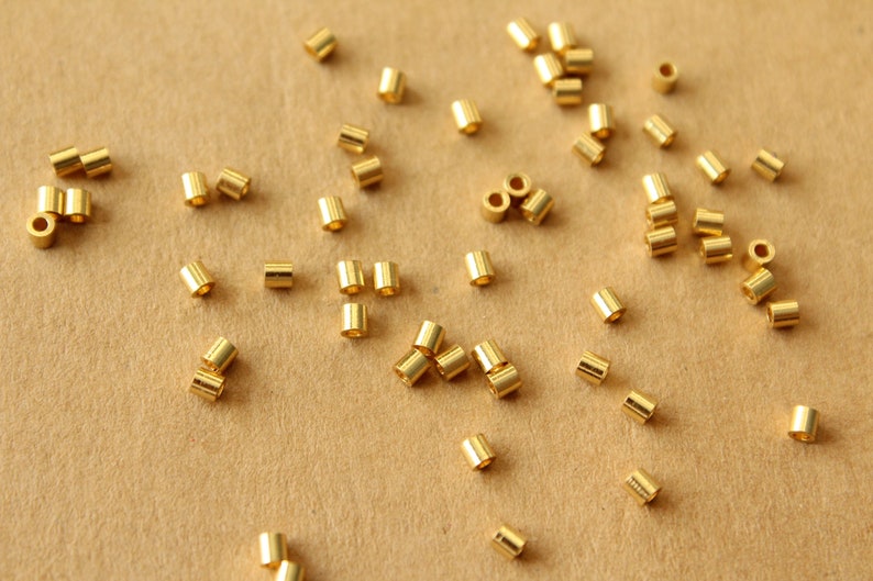 May include: A scattering of gold-colored metal jump rings on a brown surface.