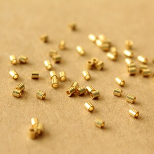 May include: A close-up of a group of gold jump rings scattered on a brown surface. The jump rings are small and round, with a hole in the center. They are used for connecting jewelry pieces together.